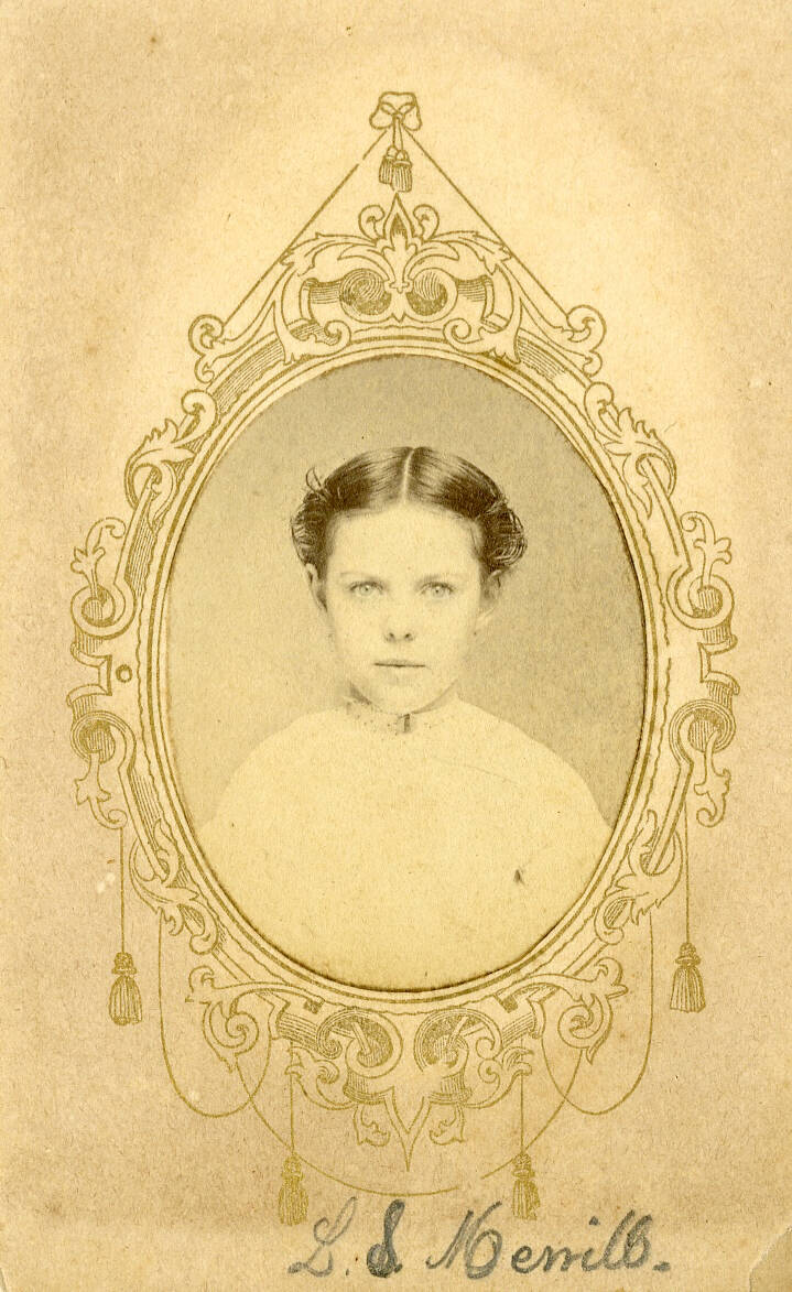 Black and white carte de visite photograph of a young girl in a light colored dress. Drawn frame around oval image, handwritten name at bottom.